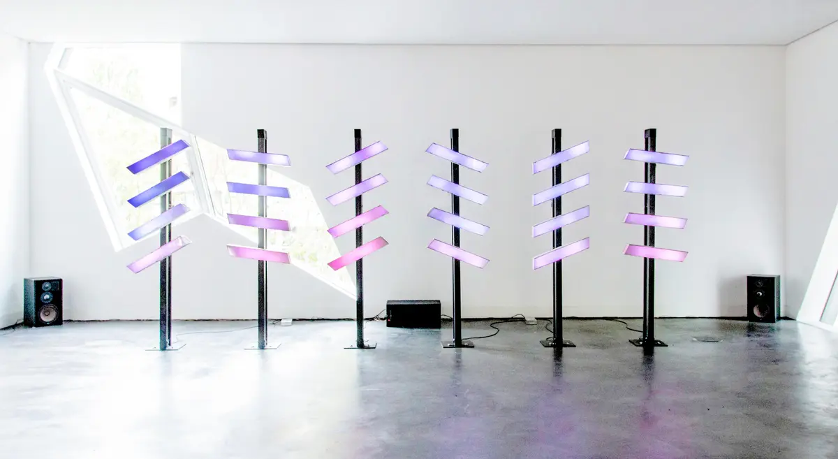 six steles with 5 light bars horizontally attached are standing in a white room. featured